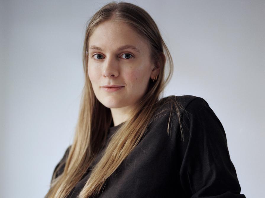 Kvinde med langt hår og en sort bluse sidder og ser ind i kammaret